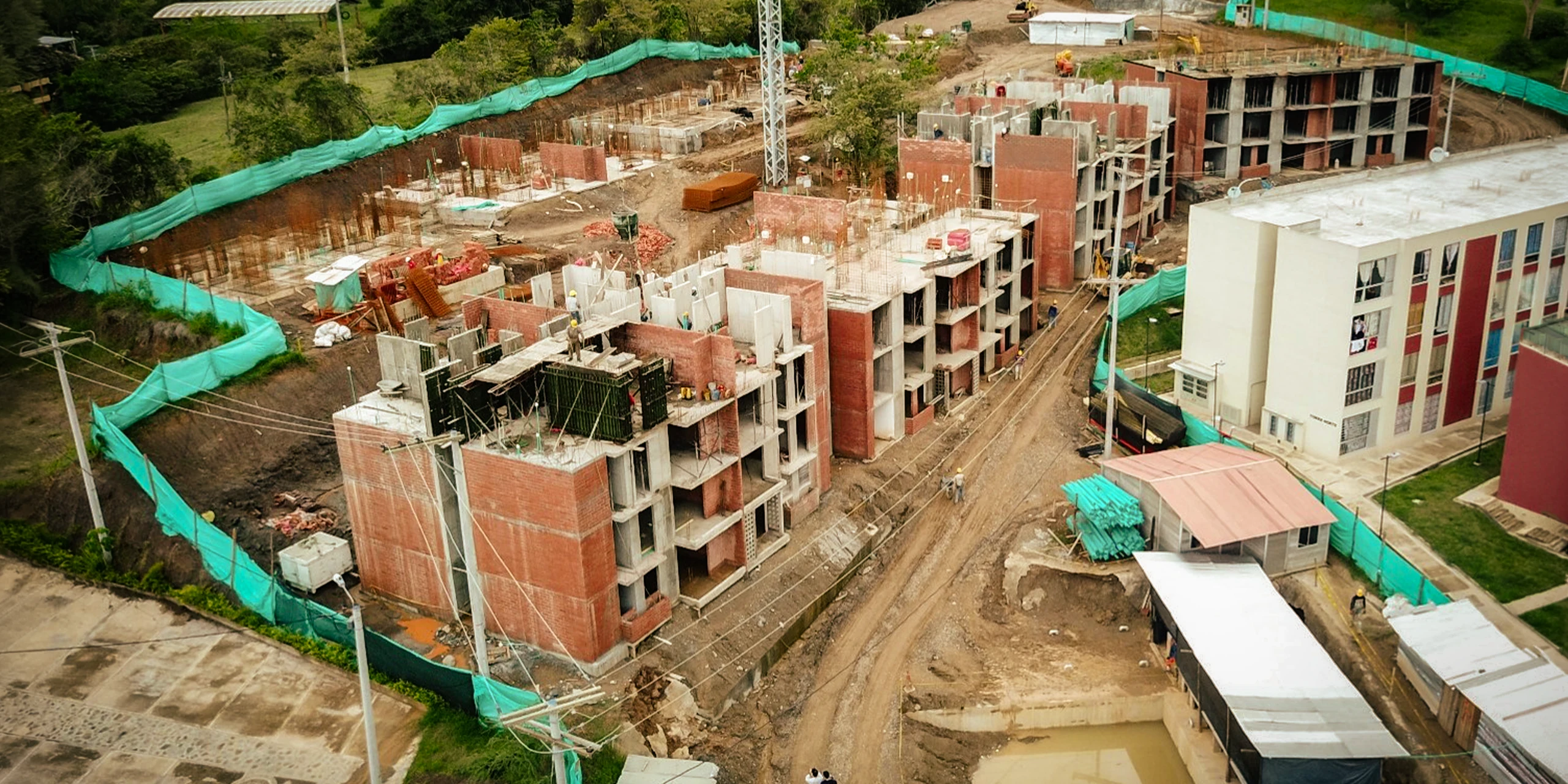 The site from above: concrete walls cast in place advance in stages down the hillside, next to the first finished blocks.