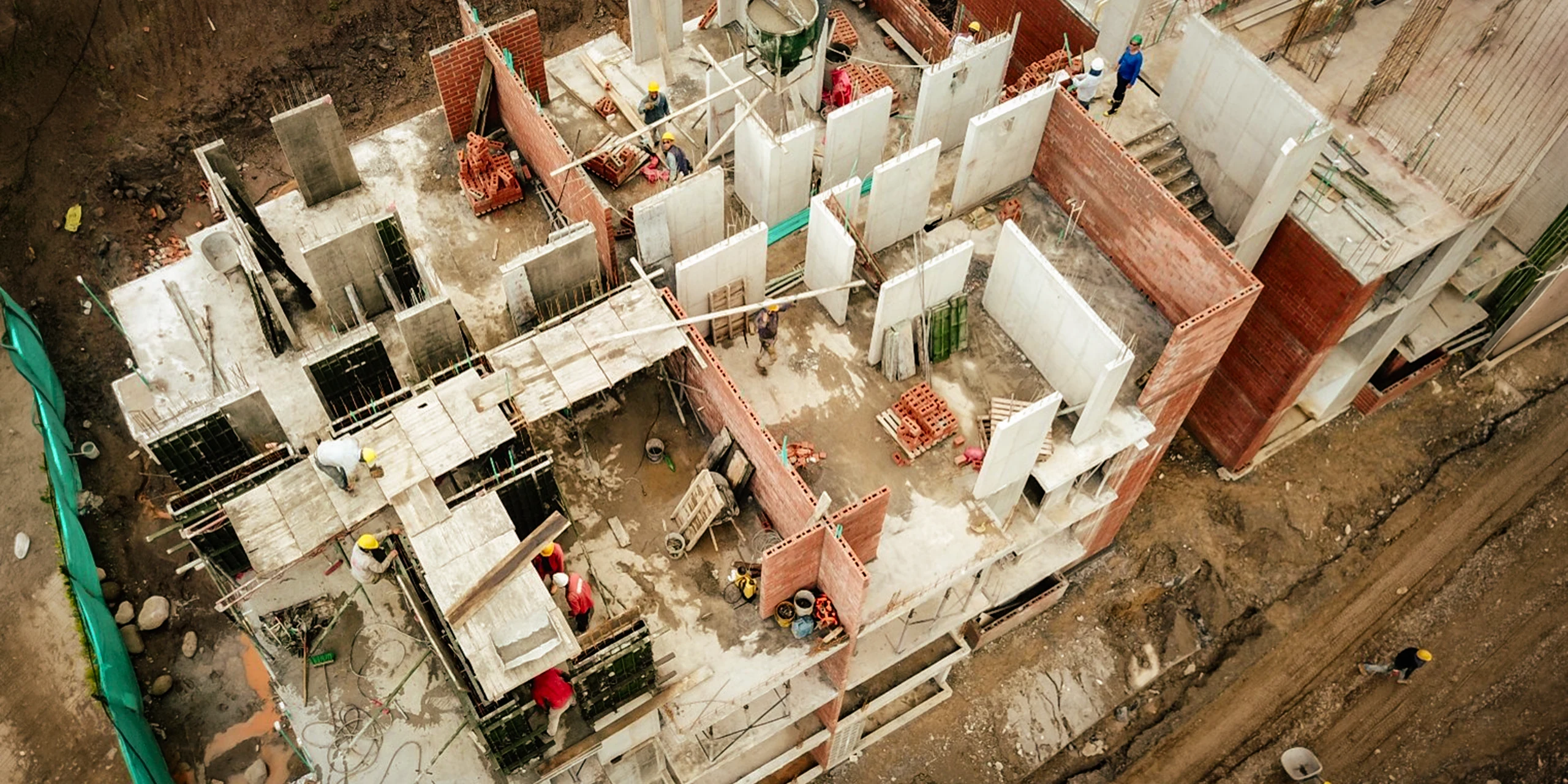 Building system up close: metal formwork, load-bearing concrete walls and brick enclosures rising over the slab.